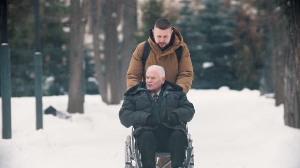 A Young Man Walking Outdoors with His Grandfather in Wheelchair