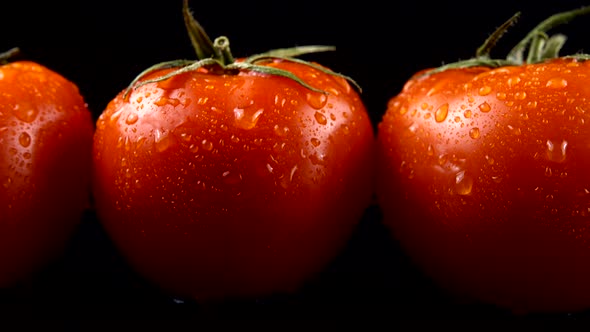 Red tomatoes on a black background in water drops