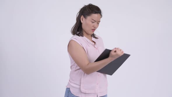 Young Serious Asian Businesswoman Showing Clipboard and Giving Thumbs Down