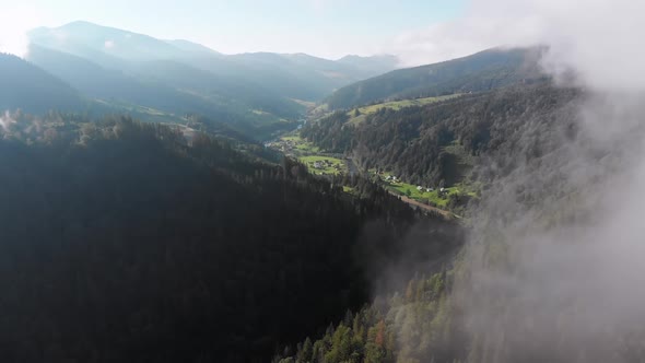 Flying Through the Clouds Over Carpathian Mountain Valley with Village in Summer