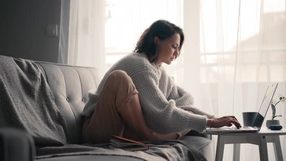 A Young Woman Typing on a Laptop and Checking Messages on a Smartphone