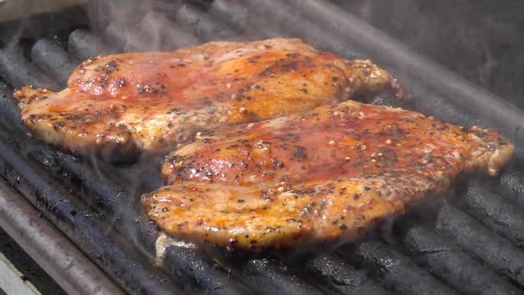 Grilling pork steaks. Delicious marinated meat steaks cooking on the grill. Slow motion 240 fps