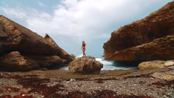 Moving handheld toward beautiful real woman in bikini standing on ocean rock