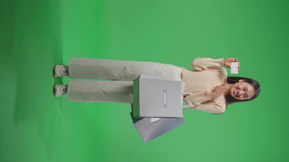 Full View Of Woman With Shopping Bags Holding And Pointing A White Card Smile At Green Screen