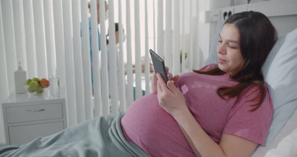 Happy Pregnant Woman Lying in Hospital Bed Using Digital Tablet