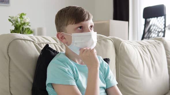 A Young Boy in a Face Mask Thinks About Something As He Sits on a Couch at Home - Closeup