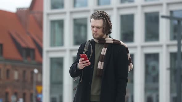 stylish guy in scarf and coat hold mobile phone in a hand at street of Wroclaw, Poland