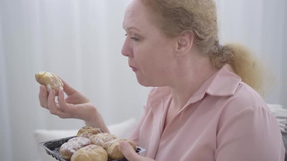 Close-up Side View of Chubby Senior Woman Chewing Sweet Bun. Portrait of Redhead Caucasian Lady