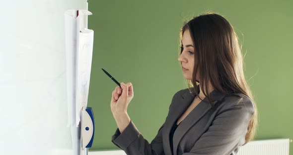 Beautiful Young Business Woman Performs Financial Calculations on Presentation Whiteboard, Working