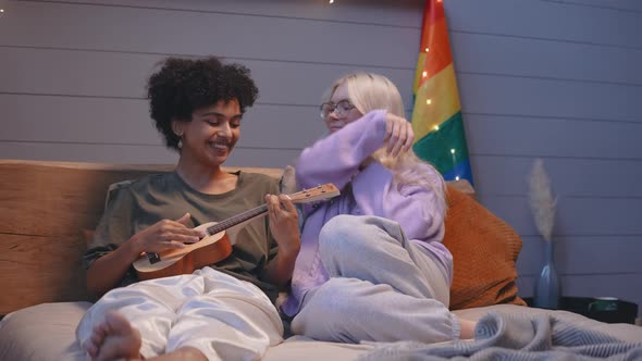 A Young LGBT Couple Lies in Bed in the Evening and Plays the Ukulele Hugging