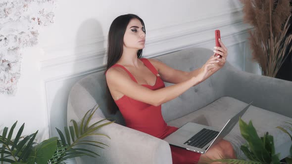 Beautiful Young Brunette Woman Using Laptop and Making Selfie on Smartphone