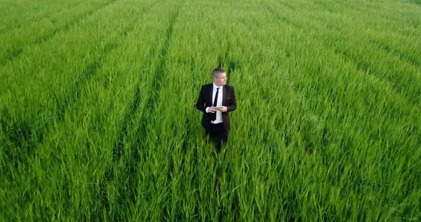 A Young Agronomist in Business Clothes Inspects a Green Field