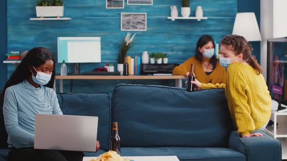 African Woman with Face Mask Pointing on Laptop Sitting on Sofa