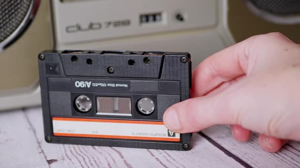 Female Hand Holds an Old Audio Cassette From the 90s Near a Stereo Tape Recorder