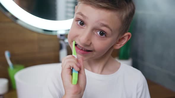 10-Aged Blond Boy Which Cleaning His Teeth and Winking at Camera After Finishing Brushing alt