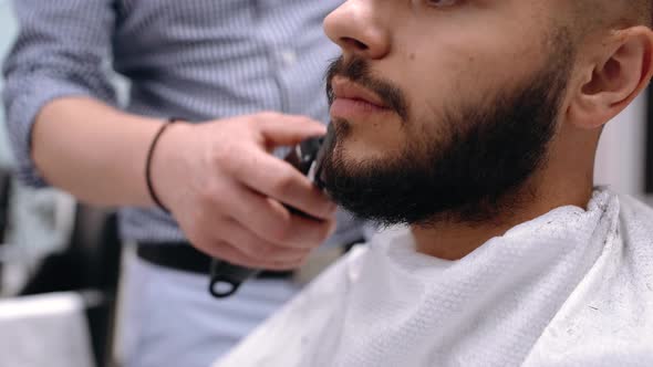 Unparalleled Barber with a Beard and a Tattoo Is Cutting the Hair of His Client in the Barbershop.