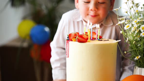 Child blowing candles on homemade baked cake, indoor. Colored party for school children