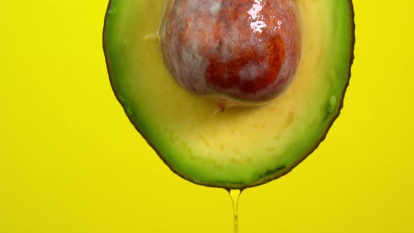 Oil flows from avocado on yellow background. Avocado slice and water splashing, drops of juice