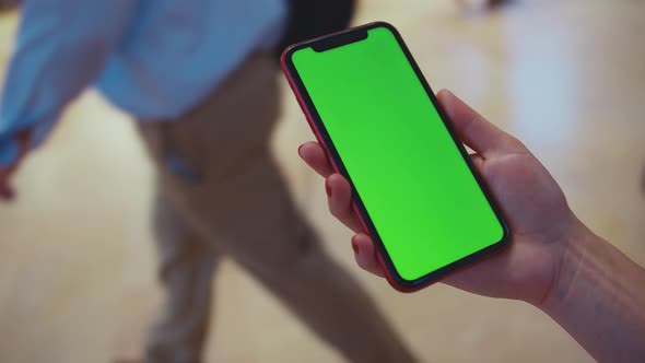 Female hand holding a smartphone with green display at a train station