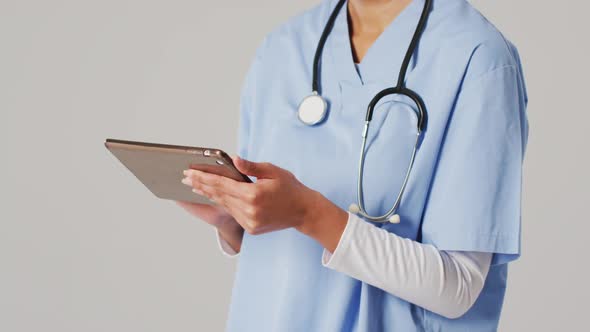 Video of biracial female doctor using tablet on blue background