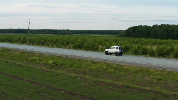 Aerial View of a Car Driving Along the Road Among Fields of Green Grass