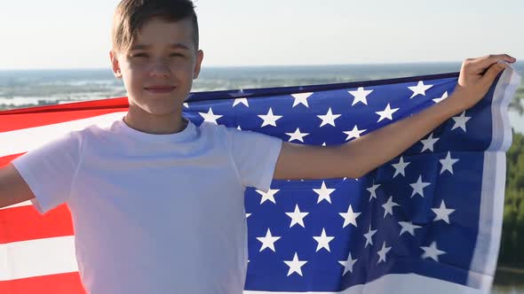 Boy Waving National USA Flag Outdoors Over Blue Sky at the River Bank