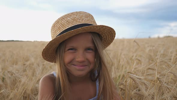 Close Up of Beautiful Smiling Girl in Straw Hat Looking Into Camera Against the Background of Barley