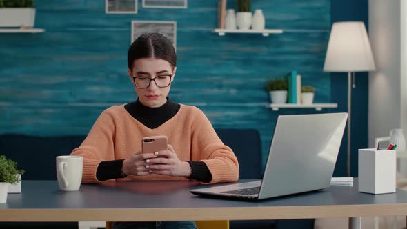 Person Sitting at Desk and Using Smartphone to Browse Internet