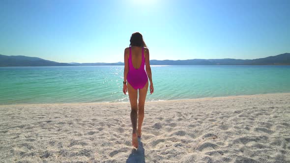 Sexy Female Model in Pink Swimsuit Walking on the White Beach of the Clear Tropical Turquoise Sea