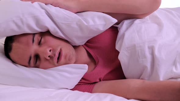 Man Trying To Sleep Annoyed By Bad Noisy Room Neighbors Covering Ears with Pillow