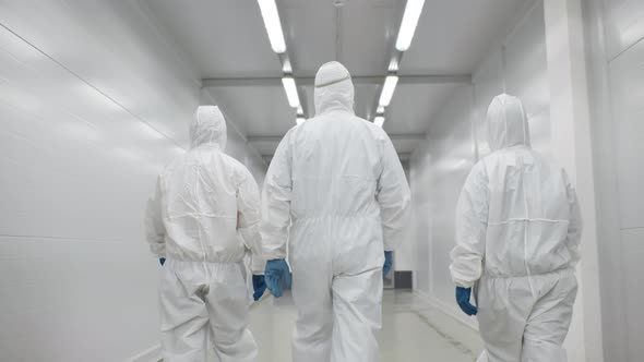 Back View of Three Disinfectors or Doctors Walk in Protective Uniform Walking in Hospital Corridor