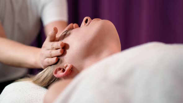 Woman masseur makes face relaxing massage to young beautiful female client blonde spa treatment