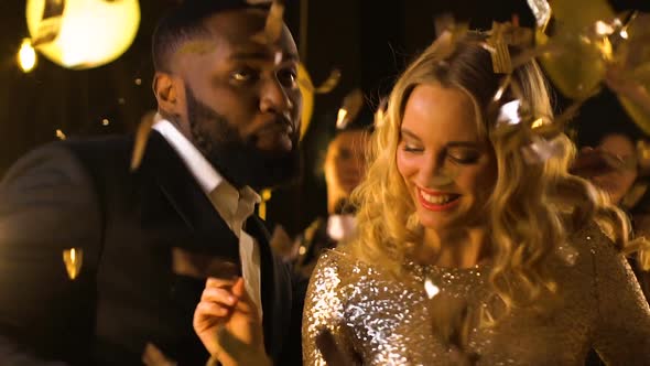 Cheerful Mixed-Race Couple Dancing at Party Under Falling Confetti, Celebration