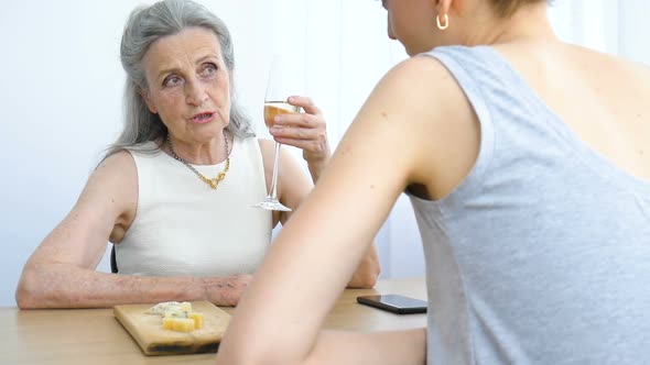 Female Portrait of Adult Daughter and Senior Mother Talking and Drinking Champagne at Home Sitting