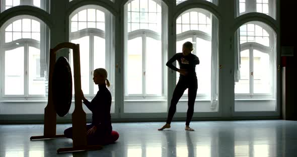 A Young Slender Blonde Girl Dancer Is in a Large Studio with Large Windows, She Approaches the Gong