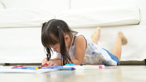 Cute adorable asian ethnic kid girl holding color pen drawing and painting, lying on warm floor, She