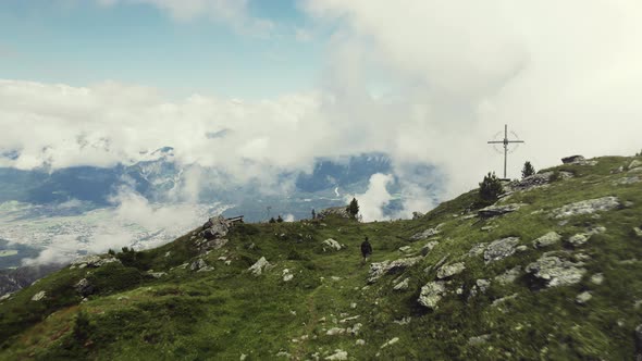 Aerial drone shot of a grass covered mountain top with a person hiking along a small trail. A valley