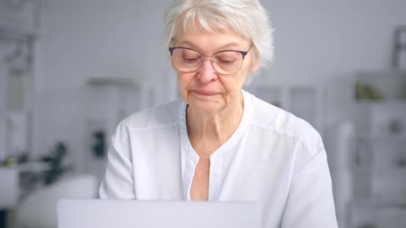 Concentrated aged businesswoman in glasses types on laptop