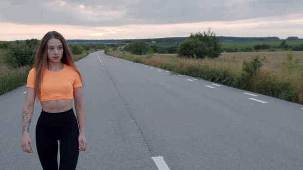 Happy Sporty Girl Walks on the Main Road During a Workout at Nature