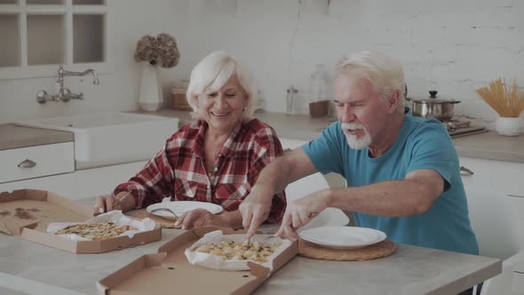 Senior Couple Sharing Takeaway Pizza In Kitchen