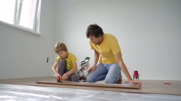 Father and His Little Son Install Laminate on the Floor in Their Apartment