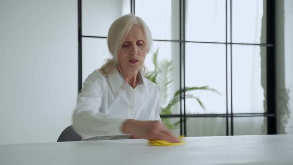 Mature Woman Wipes a Wooden Table with a Rag