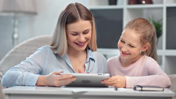 Beautiful Young Mother and Smiling Teen Daughter Looking at Screen of Tablet Pc Having Fun Together