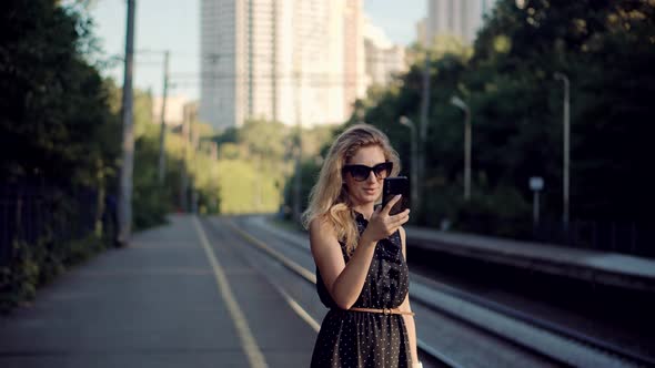 Woman Using Mobile Phone And Waiting Public Transport On Train Station. Active Lifestyle On Vacation