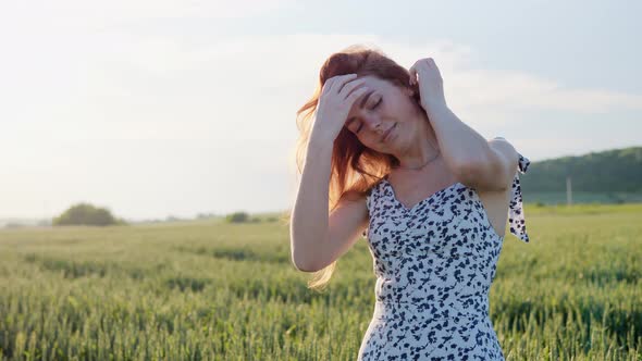 Cheerful Smiling Ginger Woman Straightens Hair in Green Wheat Field Outdoors