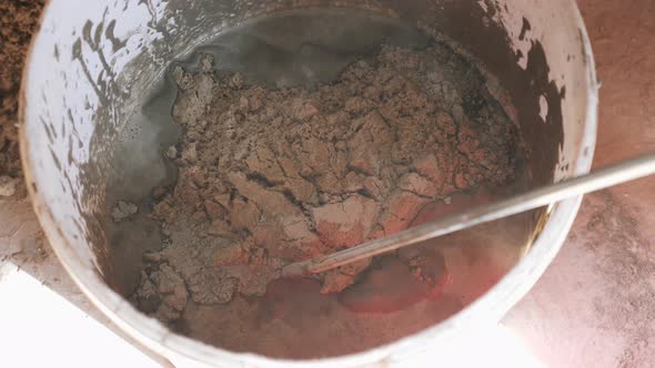 Water, sand and cement are mixed by worker in bucket