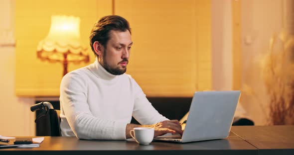 Young Handicaped Man Freelancer Using Laptop Typing Scrolling Surfing Web Looking at the Screen