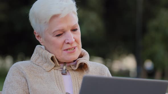 Old Lady Happy Senior Woman of Retirement Age Sitting Outdoor Making Video Call Looking at Laptop