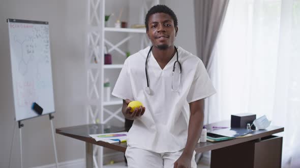 Cheerful Young African American Doctor Juggling Lemon Smiling Looking at Camera