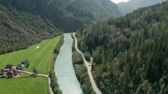 Drone Over  Sunlit River And Road By Forest And Buildings